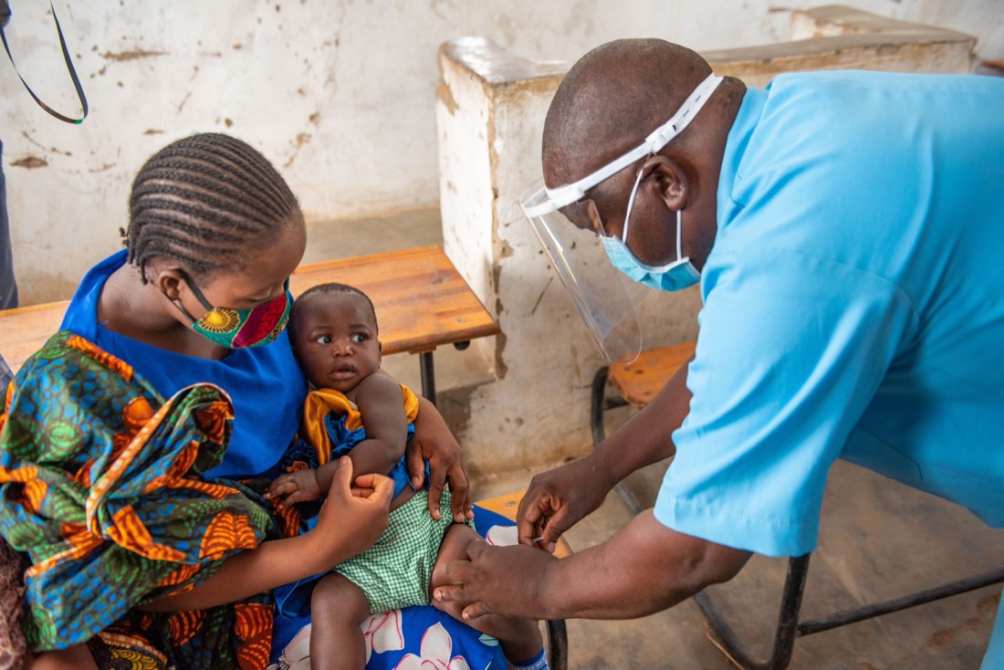 A community health worker vaccinates an infant held by their mother at a village clinic.